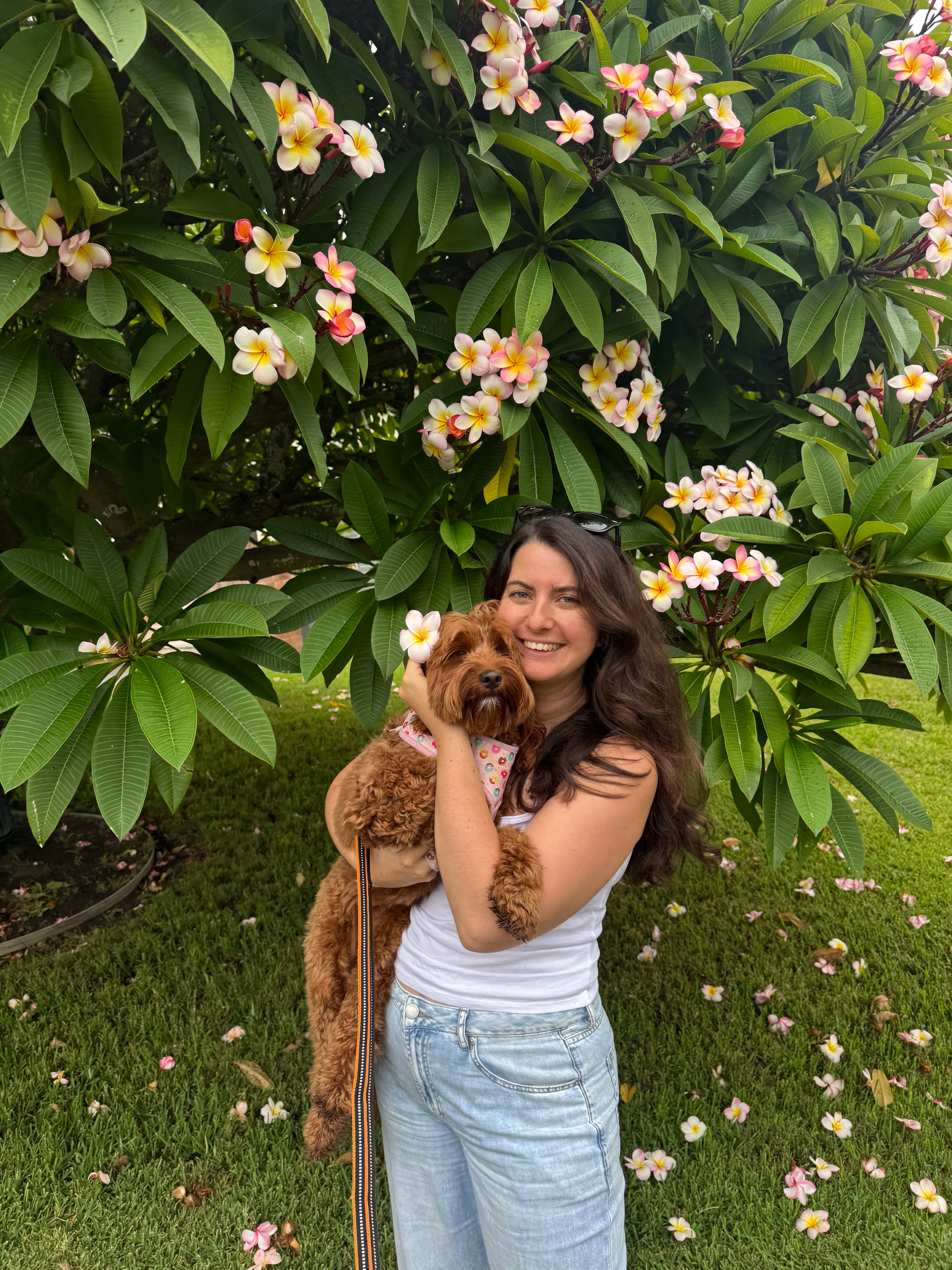 Renata smiling and holding a dog under a frangipani tree
